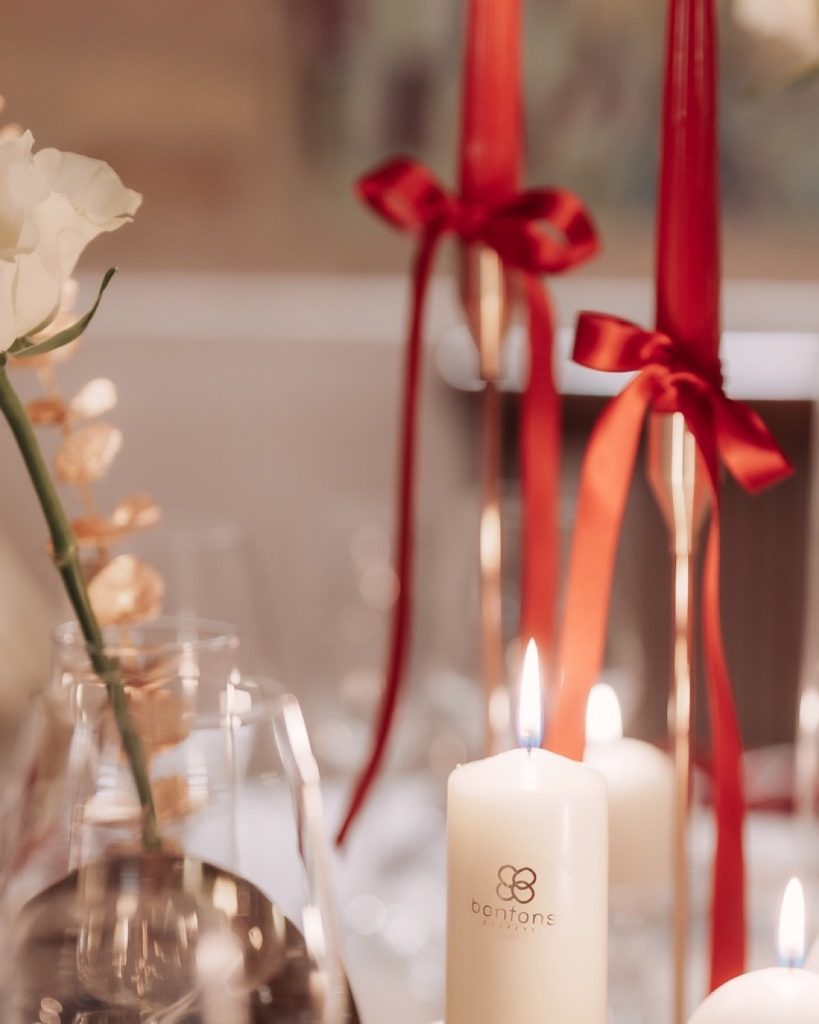 Candele rosse con fiocchi, rosa bianca e candela con il marchio Bontons