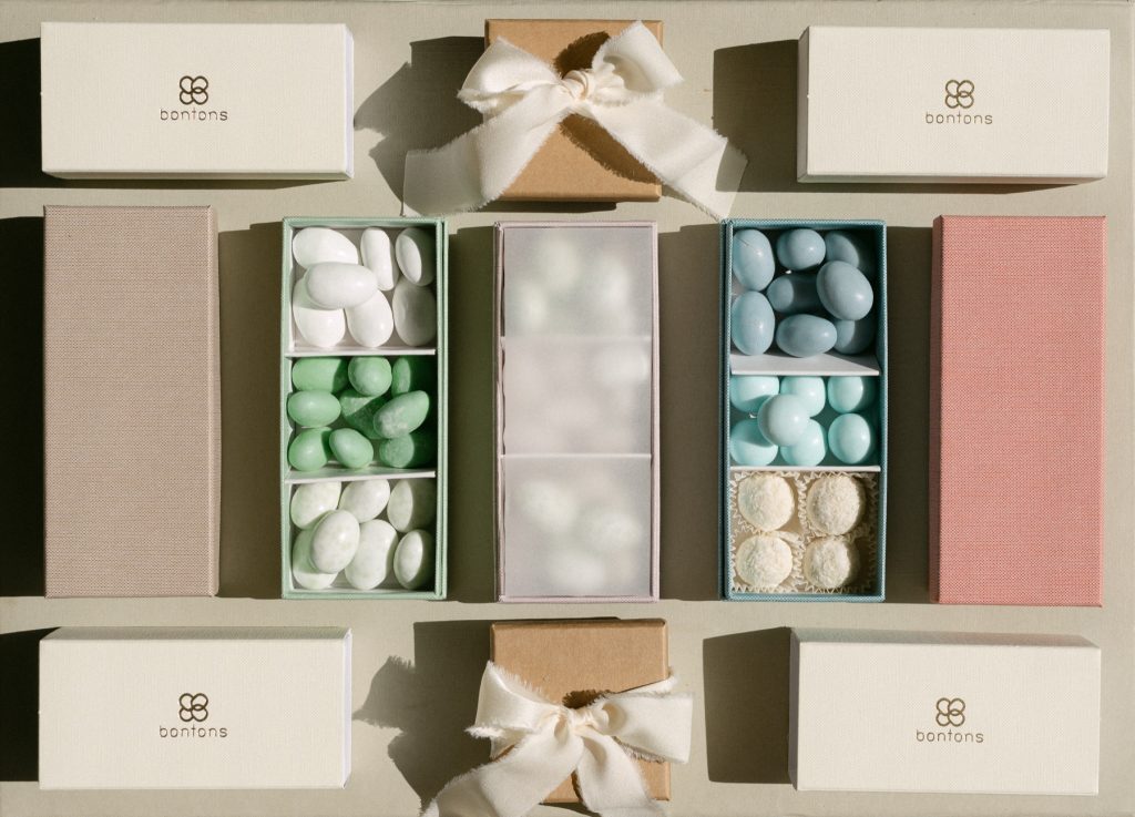 Scatole avorio con il marchio Bontons, scatoline in carta kraft con fiocco e scatole a scomparti con confetti bianchi, verdi e azzurri