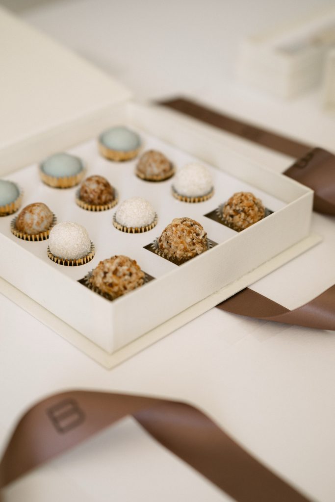 Cofanetto avorio aperto con nove praline e confetti nei pirottini e nastro marrone