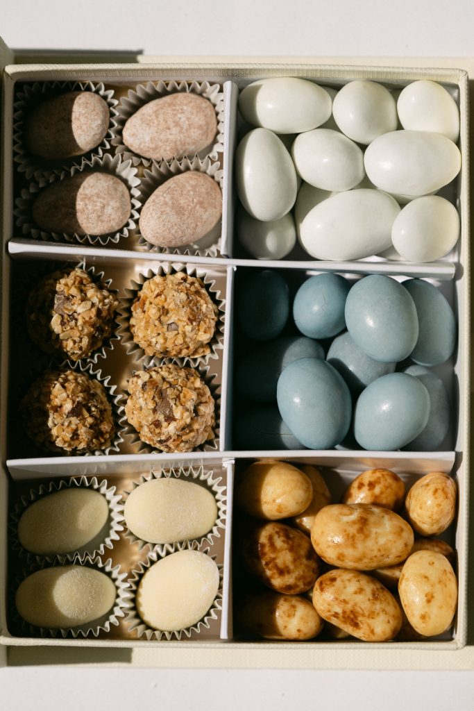 Dettaglio di un cofanetto a scomparti con confetti bianchi, azzurri e rosati e praline