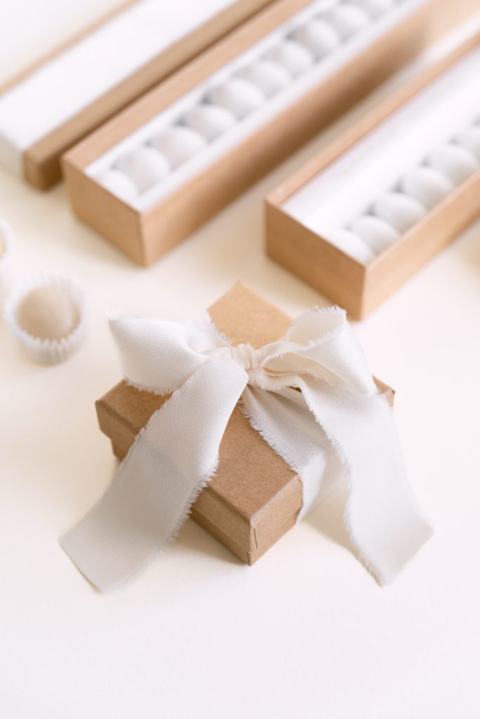Scatolina in carta kraft con fiocco avorio davanti ad astucci di confetti
