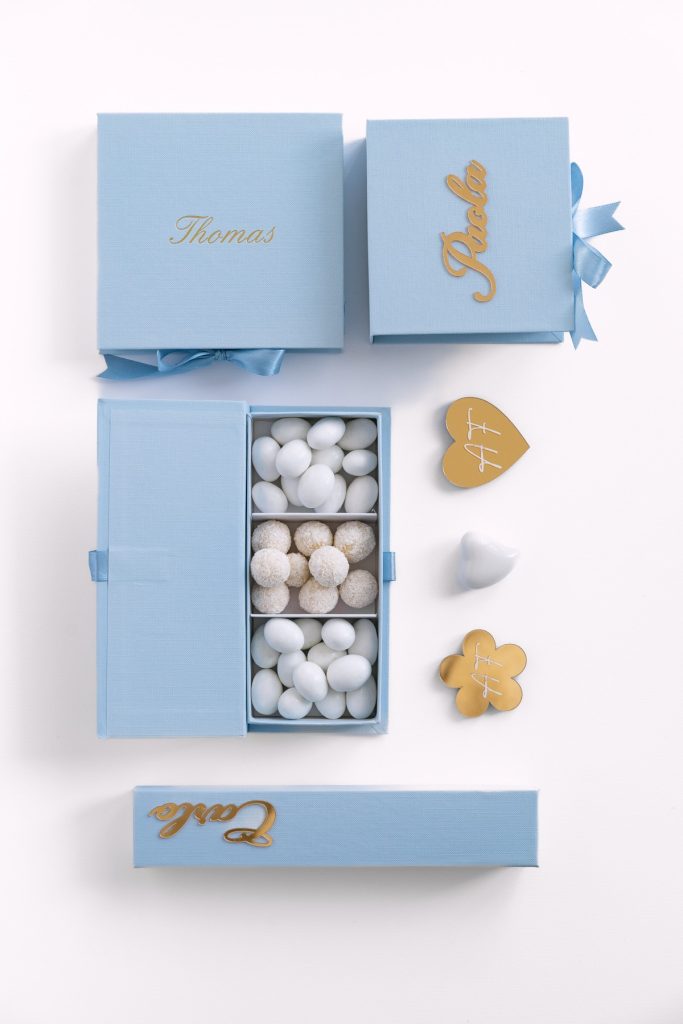 Scatole azzurre personalizzate con nomi in oro, cofanetto con confetti bianchi e decorazioni dorate a cuore e a fiore