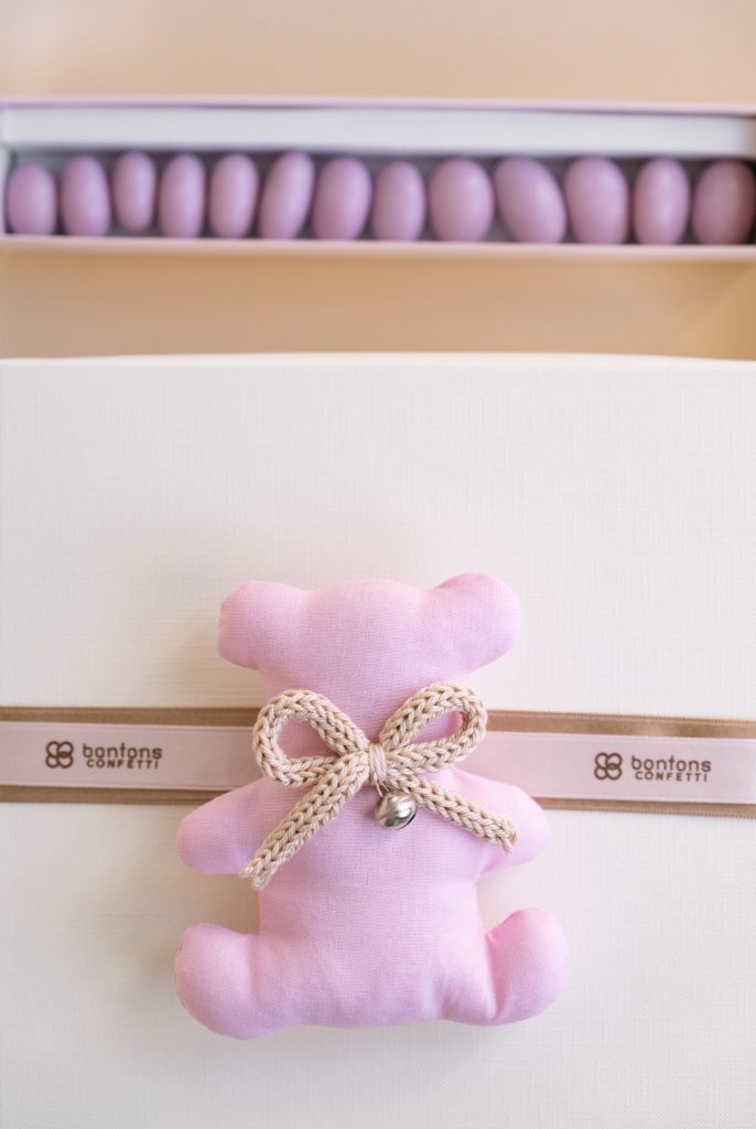 Scatola con orsetto rosa in tessuto e fascia con il marchio, sotto un astuccio di confetti rosa