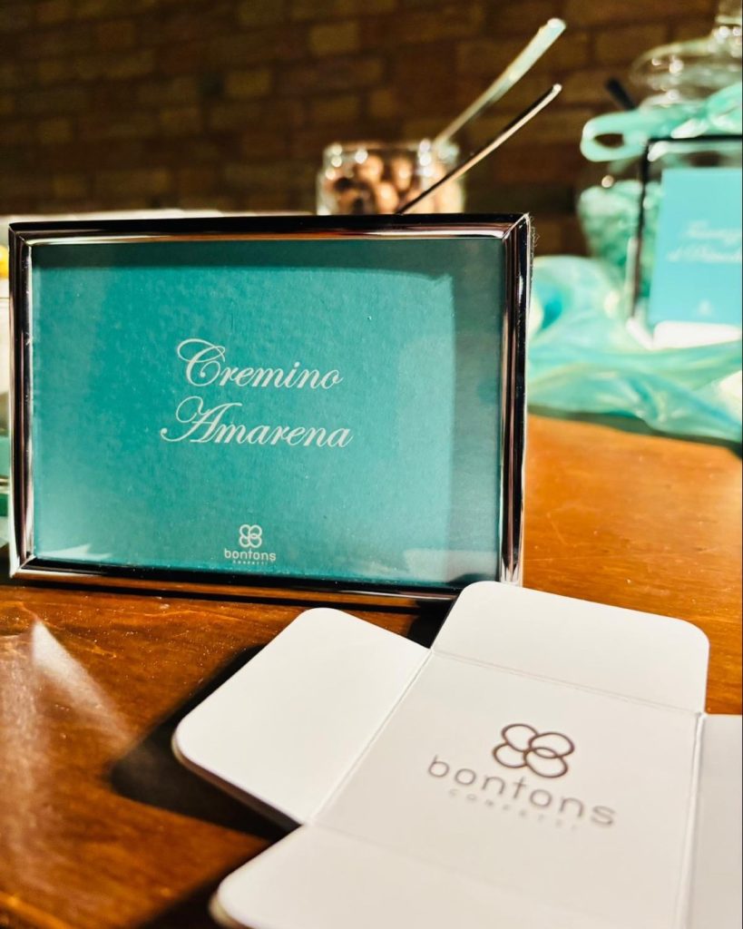 Cartoncino color Tiffany con la scritta Cremino Amarena in una cornice d’argento, davanti a un astuccio aperto con il marchio Bontons