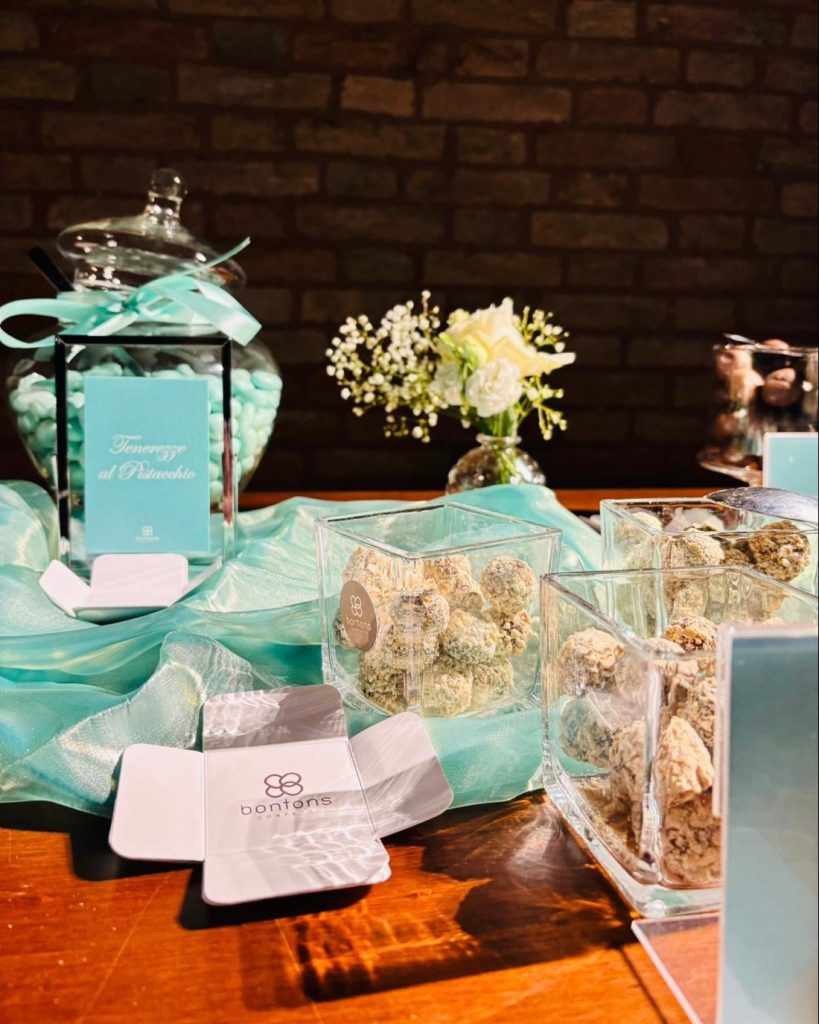 Barattolo di confetti color Tiffany con il cartoncino Tenerezze al Pistacchio, praline in cubi di vetro e un astuccio aperto con il marchio Bontons
