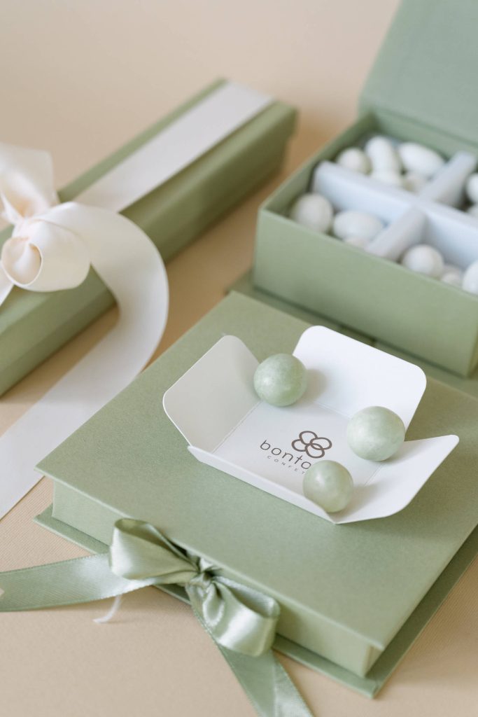 Scatole verde salvia con nastri di raso, confetti bianchi e verdi e il logo Bontons